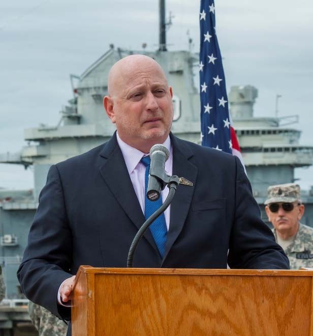 Peter Stonefield speaking at Patriots Point, with the USS Yorktown behind him